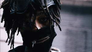 留著辮子、戴著黑色面罩的人在都市環境中戴著護目鏡。 — Scarlxrd 壁紙
