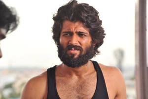 一個穿著黑色背心的鬍子男人，在戶外強烈地凝視，身後是城市天際線。 — 瓦伦·达万 壁紙