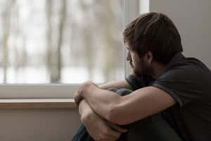一個男人坐在窗邊看著雪，顯得若有所思和悲傷。 — 孤獨 壁紙