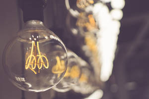 一個發光的復古燈絲燈泡，帶有溫暖的光線和柔和的背景模糊效果。 — 燈泡 壁紙