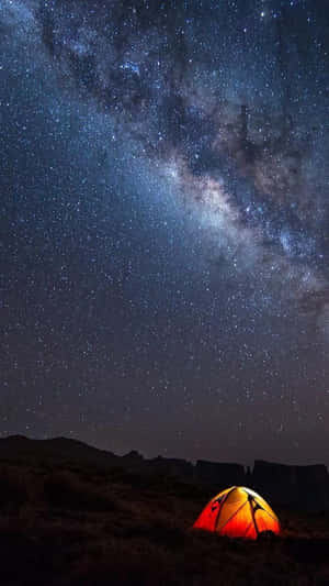 一個發光的橙色帳篷在星空夜空下，銀河可見。 — 橘色 壁紙
