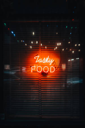 夜間穿過關閉的百葉窗發光的霓虹燈牌，上面寫著 tasty food。 — 霓虹手機 壁紙