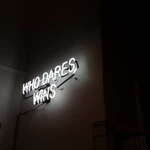 一個白色霓虹燈牌，上面寫著「WHO DARES WINS」，掛在深色牆壁上。 — iPad Pro 13 壁紙