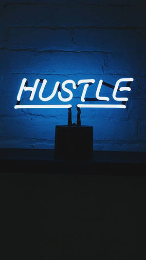 一個發光的白色霓虹燈牌，在藍色磚牆上寫著 HUSTLE。 — 深色霓虹 iPhone 壁紙