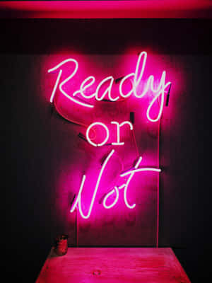粉紅色霓虹燈牌，上面寫著「Ready or Not」，掛在深色牆壁上，下方有一張木桌。 — 霓虹 壁紙
