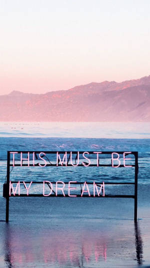 霓虹燈牌寫著「THIS MUST BE MY DREAM」，在日落時分的海水中。 — 粉紅色 壁紙
