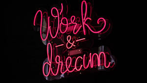 粉紅色霓虹燈牌，上面寫著 Work & Dream，置於深色反光表面。 — 美學粉色GIF 壁紙