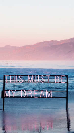 霓虹燈牌寫著「THIS MUST BE MY DREAM」，在日落時分的海水中。 — 夢幻 GIF 壁紙