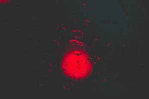 發光的紅色球體透過黑暗表面上的雨滴觀看。 — 紅色圓圈 壁紙