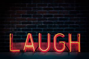 一個紅色霓虹燈牌，拼寫著 LAUGH，放在一塊木板上，靠著磚牆。 — 磚牆 壁紙