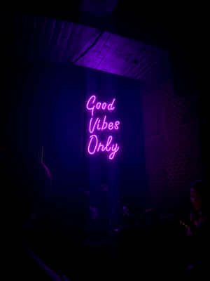 在黑暗的俱樂部環境中，一個寫著 Good Vibes Only 的紫色霓虹燈牌。 — 2048x2732 壁紙