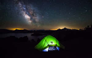 一個發光的綠色帳篷在星空下，銀河在湖泊上空。 — 海灘度假 壁紙