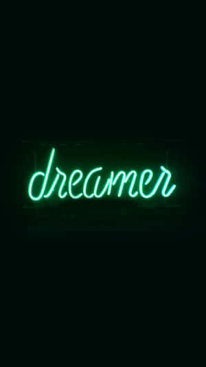 一個綠色霓虹燈牌寫著 dreamer，對著黑色牆壁。 — 深色霓虹 iPhone 壁紙