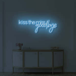 藍色霓虹燈牌，上面寫著 kiss the miss goodbye，位於一個擺放著鮮花和書籍的玄關桌上方。 — 再見 壁紙