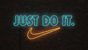 夜間磚牆上顯示「JUST DO IT」和勾號的霓虹燈牌。 — 就去做吧 壁紙