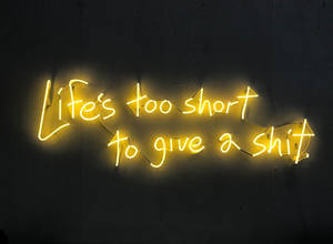 黃色霓虹燈牌在深色牆上顯示 Life's too short to give a shit。 — 螢光黃 壁紙