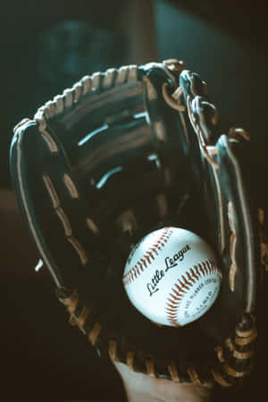 一隻手在深色皮革手套中握住一個Little League棒球。 — iPhone Duo 壁紙