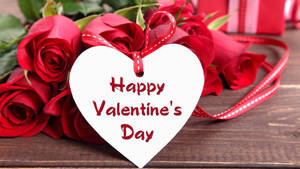 寫著 Happy Valentine's Day 的心形標籤，被紅玫瑰和絲帶環繞在木頭上。 — 白色愛心 壁紙