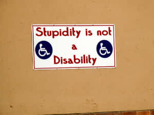 一個諷刺標牌，寫著「Stupidity is not a Disability」，帶有輪椅圖標。 — 白痴 壁紙