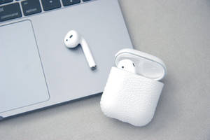 白色無線耳塞和充電盒在筆記型電腦鍵盤上。 — MacBook Air 壁紙