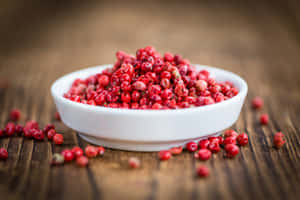 一個白色陶瓷碗裝滿紅色胡椒粒，放在木桌上。 — 美學粉色GIF 壁紙
