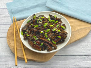 一盤釉面鰻魚配蔥花和芝麻，放在木板上，配有筷子。