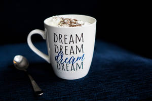 白色馬克杯有dream字樣和鮮奶油，深藍色布料上放有湯匙。 — 咖啡美學 壁紙