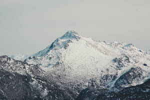 灰色天空下積雪的山峰與岩石斜坡 — 雪山 壁紙