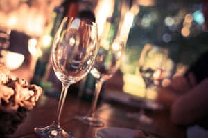 餐廳桌子上的空酒杯，背景有柔和發光的燈光。 — 慶祝 壁紙