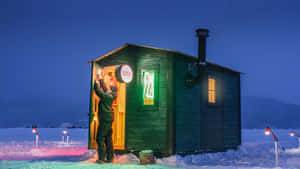 夜晚，一個人打開積雪覆蓋的小屋門，室內有溫暖燈光。 — 冬季風景 壁紙