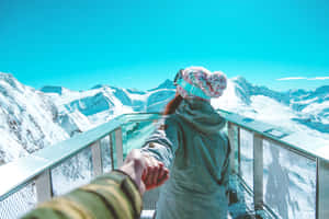 在玻璃陽台上與伴侶牽手，俯瞰日落時分積雪的山脈。 — 寒冷 壁紙