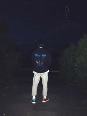 穿連帽衫的人夜晚獨自站在星空下，周圍有樹木 — Vlone 壁紙
