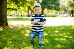一個戴著帽子和條紋襯衫的微笑幼兒，站在陽光充足的公園草地上。 — MacBook Air M4 壁紙