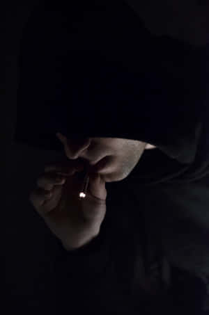 穿著深色連帽衫的人在昏暗光線下點煙 — 難過表情符號 壁紙