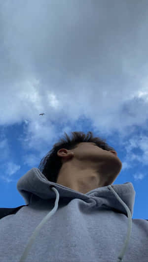 穿著灰色連帽衫的年輕男子抬頭看著有雲和飛鳥的藍天。 — 美學 壁紙