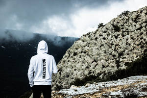 穿著白色連帽衫的人站在山上俯瞰迷霧山谷。 — Hollister 壁紙