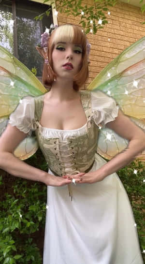 一個打扮成仙女、帶有翅膀和花卉配飾的人站在戶外。 — 仙女美學 壁紙