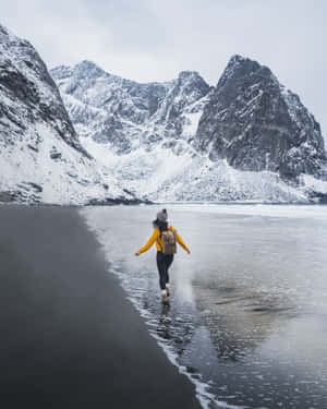 一個人沿著黑色海灘行走，背景是白雪覆蓋的山脈。 — 冬季風景 壁紙