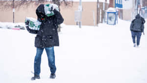 冬天城市人行道上，一個人在雪中扛著飲用水箱。 — 酷寒冬季 壁紙