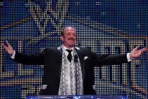 穿西裝和蛇皮領帶的男人站在講台上，雙臂張開，身後有LED燈光。 — WWE GIF 壁紙