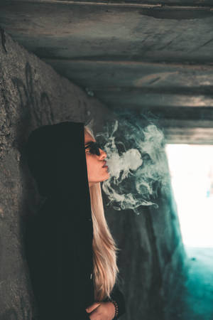 穿著黑色連帽衫和太陽眼鏡的人，在一個佈滿塗鴉的地下道中呼出煙霧。 — 抽菸 壁紙