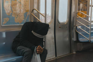 一個穿著連帽衫的人沮喪地坐在地鐵車廂的長椅上，拿著一個塑膠袋。
