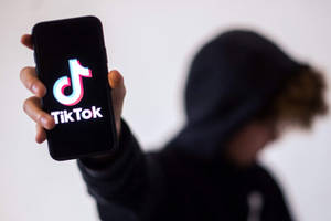 穿著黑色連帽衫的人手持顯示TikTok標誌的手機。 — 社群媒體 壁紙