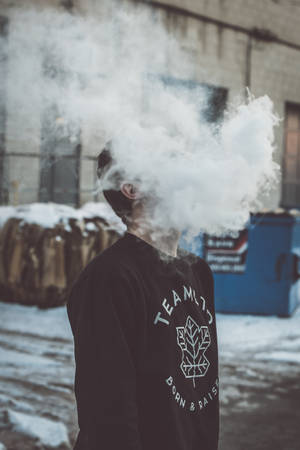 在雪白城市環境中穿著黑色運動衫呼出蒸氣的人 — 抽菸 壁紙