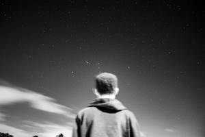 穿連帽衫的人仰望星空和移動的雲層。 — 星星 壁紙