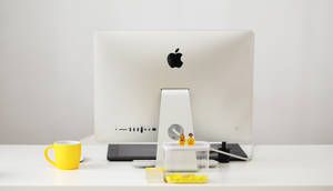 乾淨的白色桌面，配有 Apple iMac、黃色馬克杯和 LEGO 人偶。 — 極簡美學桌面 壁紙