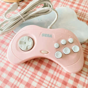 一個粉紅色Sega Genesis手把放在格紋布上，附有雲形物體。 — 粉嫩粉彩美學 壁紙