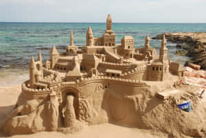 一個詳細的沙堡，帶有塔樓和橋樑，位於陽光普照的海灘上，靠近海洋。 — 海灘 壁紙