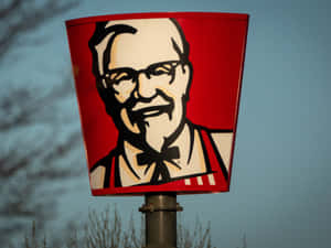 KFC桶形招牌，桑德斯上校臉孔，背景黃昏天空和光禿樹木。 — 肯德基 壁紙