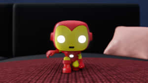 紅色和金色的鋼鐵人Funko Pop人偶，在黑色沙發附近的紅色紋理表面上。 — 鋼鐵人標誌 壁紙